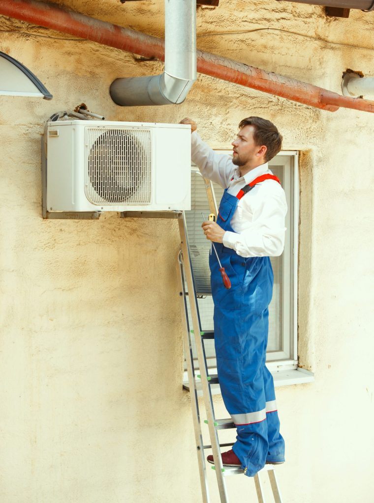 HVAC technician working on a capacitor part for condensing unit. Male worker or repairman in uniform repairing and adjusting conditioning system, diagnosting and looking for technical issues.